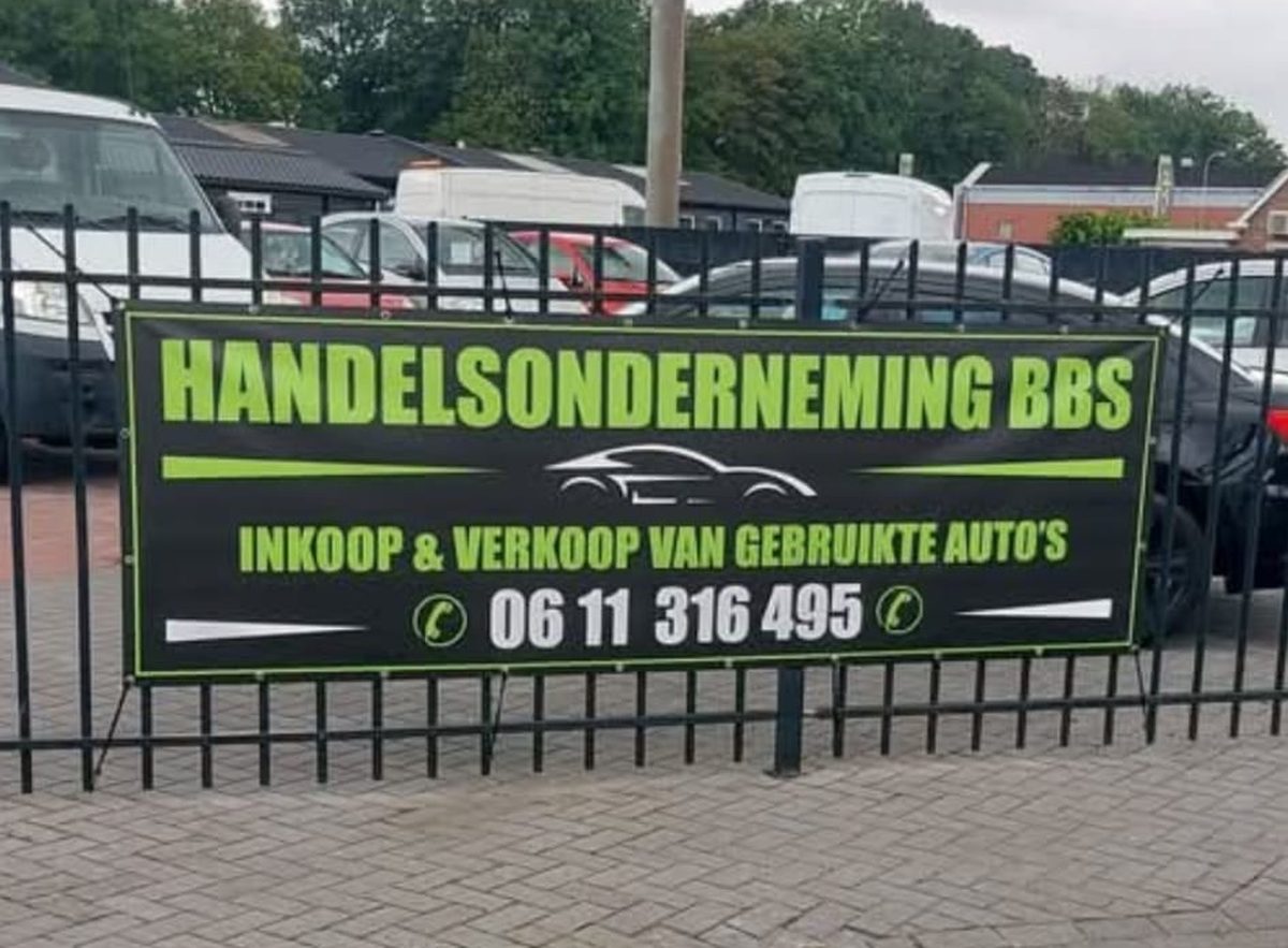 Banner van Handelsonderneming BBS op het hek aan Pekelwerk in Nieuwe Pekela, met auto's op het terrein
